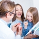 A dentist shows a dental model to a smiling young girl and a woman, likely her mother, in a dental office.