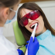 A dentist in gloves uses a dental tool to clean a womans teeth; the woman wears protective eyewear and a dental bib.