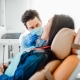 A dentist wearing gloves and a mask examines a patient who is reclining in a dental chair in a brightly lit clinic.
